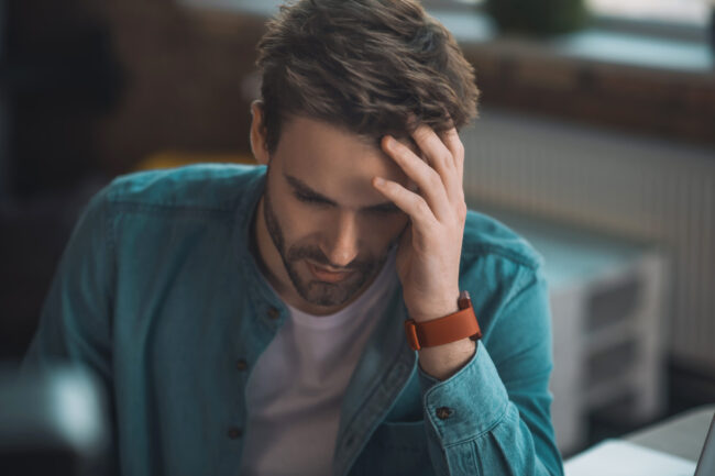 Handsome sad young man touching his head Man at work